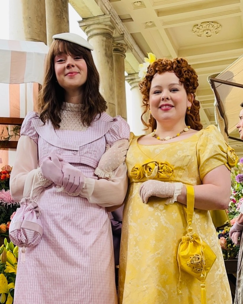 Eloise e Penelope usando vestidos lilás e amarelo respectivamente